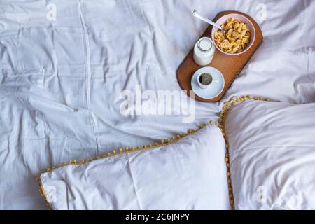 Simple Breakfast in bed with corn flakes, milk and coffe on wooden desk. Yellow and white colors. Flat lay, copy space Stock Photo