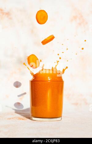 Fresh Carrot slices falling in a glass with carrot juice. splash in glass on a light background Stock Photo