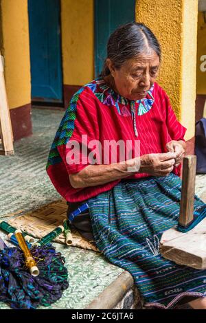 Guatemala, Solola Department, Santa Cruz la Laguna, An older Mayan woman in traditional dress winds thread in preparation for weaving on a back loom. Stock Photo