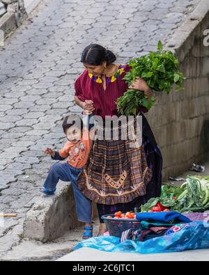 Guatemala, Solola Department, Santa Cruz la Laguna, A Cakchiquel Mayan mother in traditional dress helps her young son. Stock Photo