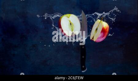 The sliced Red apple and A kitchen knife are floating in the air with water splash, the image stopped moving on dark blue background. Minimalism conce Stock Photo