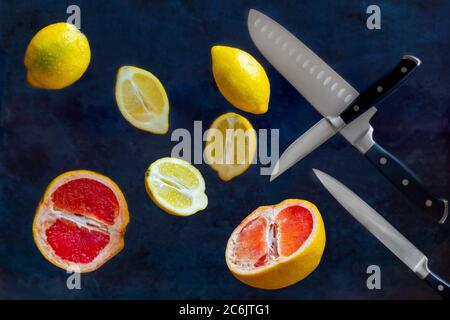 The sliced lemons, grapefruit and kitchen knives are floating in the air, with the image stopped moving on dark blue background. Stock Photo