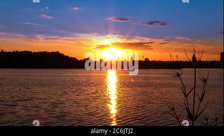Amazing sunrise over a lake. Rays of the sun reflecting on the water. Silhouette of vegetation in the foreground. Stock Photo