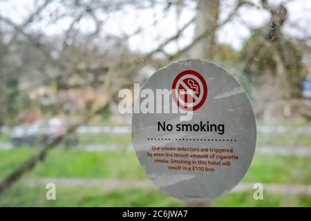 Shallow focus of a hotel No Smoking Sticker seen within a room's window. Cars can be seen in the distant next to a busy road junction in London. Stock Photo