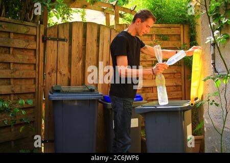 Person performing a selective sorting of household waste in recycling bins. Man putting plastic bottles in a yellow container and garbage in a bag in Stock Photo