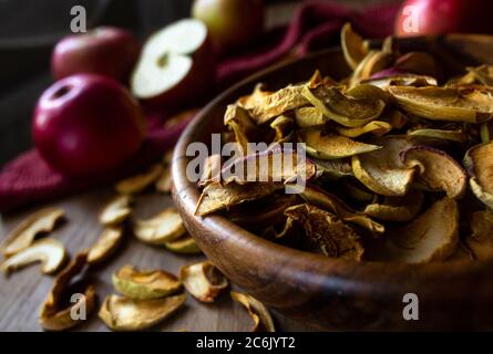 Homemade sun-dried organic apple slices in a bowl and fresh ripe red apples on an old rustic wooden table Stock Photo