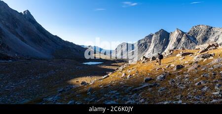 A backpacker pauses on the ascent of Raid/Bonneville Pass to view the sun rising over the peaks to the east. Wind River Range, Wyoming. Stock Photo