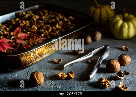 Whole and halved walnuts in pan with Nutcracker and pumpkins on a dark background. Stock Photo