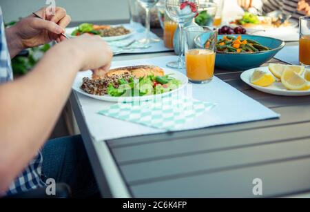 Close up photo of hands young man eating fresh salad, quinoa and fish with family on terrace at home Stock Photo