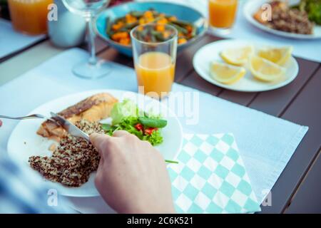 Close up photo of hands young man eating fresh salad, quinoa and fish with family on terrace at home Stock Photo