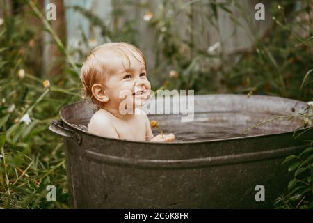 Cute funny little boy bathing in galvanized tub outdoor in green garden ...