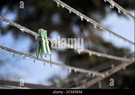Two clothes pegs on clothes line.  Pegs and line are covered with ice.  Blurry background. Vertical shot with copy space in right part of image. Stock Photo