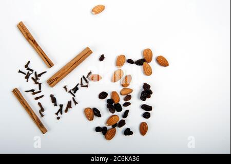 Cloves, cinnamon sticks, raisins and almonds spread out on white surface.  Top view angle. Horizontal photo with copy space on right side of image. Stock Photo