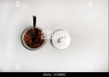 Jar with brown sugar. A spoon is standing in the jar, and the lid is on the side.  White background, top view angle. Stock Photo
