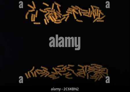 Two rows of randomly placed pasta screws in upper and lower part of horizontal image.  Black background. Copy space on the sides and in the middle of Stock Photo