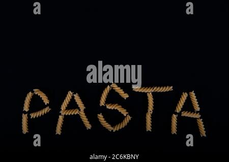 The word pasta written with pasta screws.  Copy space in upper part of horizontal image.  Black background. Stock Photo