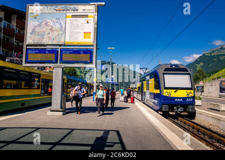 Grindelwald, Switzerland - July 30 2019 : Train of the Berner Oberland Bahn waiting in the railway station. Passengers with backpacks and luggage on t Stock Photo