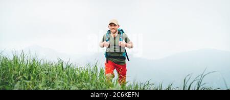 Smiling backpacker walking by the foggy cloudy weather mountain range path with backpack. Active sport backpacking healthy lifestyle concept. Stock Photo