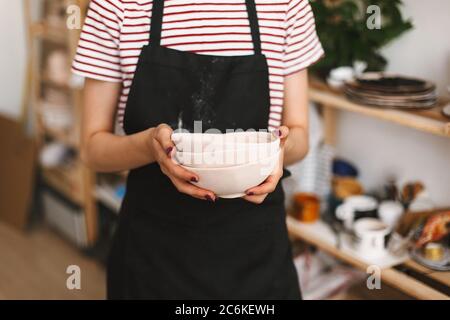 Close up of girl holding handmade bowls in hands over black apron at pottery studio. Stock Photo