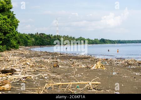 balinese fishermen (angler) on a tropical beach with pile of waste discharged by sea Stock Photo