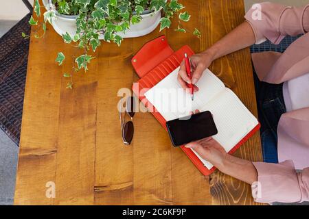 Woman hands writing on an orange agenda and holding cell phone Stock Photo