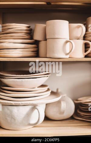 Close up handmade classic clay dishes on wooden shelves at pottery studio isolated. Stock Photo