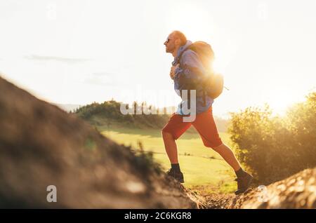 Backpacker traveler in trekking boots jumping over the ditch on mountain dirty path at summertime sunny day side shot image. Stock Photo