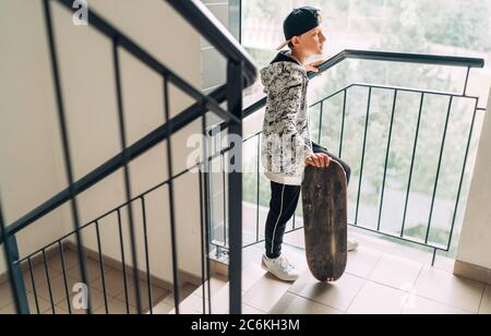 Teenager skateboarder boy with a skateboard going up by staircase home. Youth generation Freetime spending concept image. Stock Photo