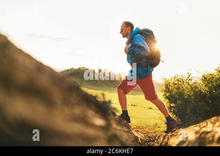 Backpacker traveler in trekking boots jumping over the ditch on mountain dirty path at summertime sunny day side shot image. Stock Photo