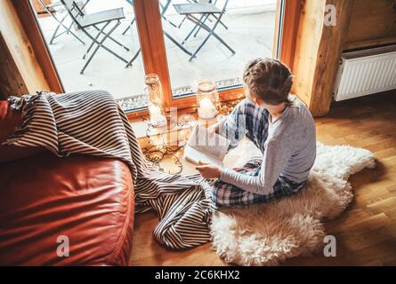 Boy reading book on the floor on sheepskin in cozy home atmosphere. Peaceful moments of cozy home concept image. Stock Photo