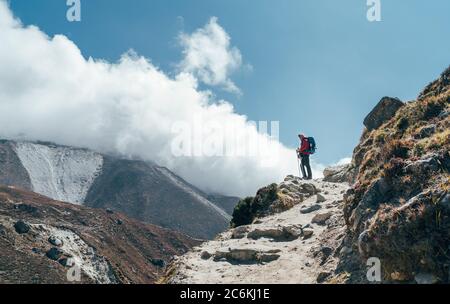 Hiker man silhouette on clouds background standing on path going over the Imja Khola valley and enjoying mountain views during an Everest Base Camp tr Stock Photo