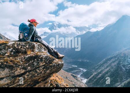 Young hiker backpacker female sitting on cliff edge and enjoying the Imja Khola valley during high altitude Everest Base Camp (EBC) trekking route nea Stock Photo