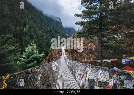 Suspension Bridge decorated with multicolored Tibetan Prayer flags hinged over gorge.  Everest Base Camp (EBC) trekking route, Sagarmatha National Par Stock Photo