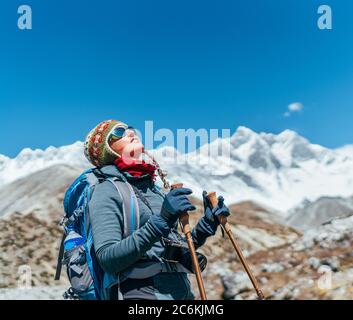 Young hiker backpacker female taking brake in hike walking during high altitude Everest Base Camp (EBC) route with snow Himalayan peaks on background. Stock Photo
