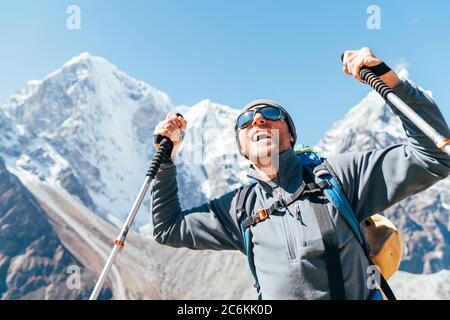 Portrait of smiling Hiker man on Taboche 6495m and Cholatse 6440m peaks background with trekking poles, UV protecting sunglasses. He enjoying mountain Stock Photo