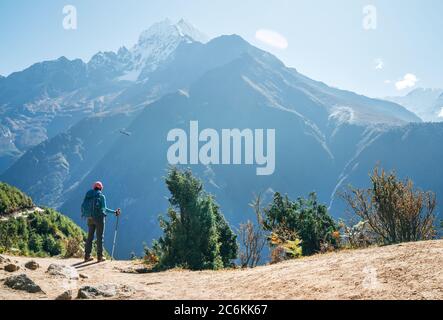 Young hiker backpacker man using trekking poles enjoying the Thamserku 6608m mountain with flying rescue helicopter during high altitude Acclimatizati Stock Photo