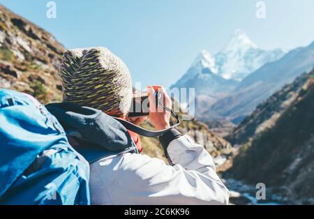 Young hiker backpacker female taking photo mountain view during high altitude Acclimatization walk. Everest Base Camp trekking route, Nepal. Active va Stock Photo