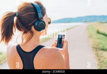 Young teenager girl starting jogging and listening to music using smartphone and wireless headphones. Active sport life concept image. Stock Photo