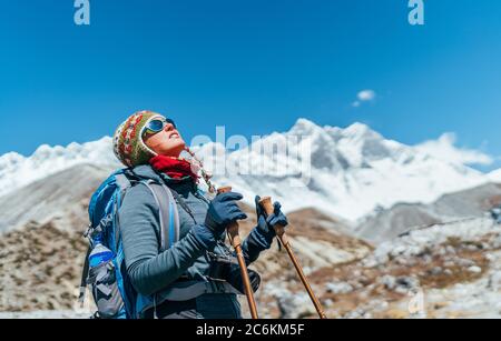 Young hiker backpacker female taking brake in hike walking during high altitude Everest Base Camp (EBC) route with snow Himalayan peaks on background. Stock Photo