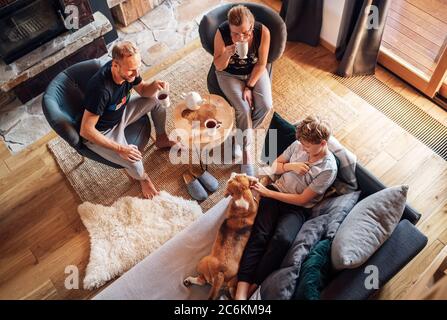 Cozy family tea time. Father, mother and son  at the home living room. Boy lying in comfortable sofa and  stroking their beagle dog and smiling. Peace Stock Photo