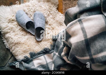 The pair of gray home slippers near the  bed on the white sheepskin in the cozy bedroom. Home sweet home concept top view image. Stock Photo