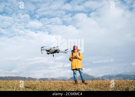 Teenager boy dressed yellow jacket piloting a modern digital drone using remote controller Stock Photo