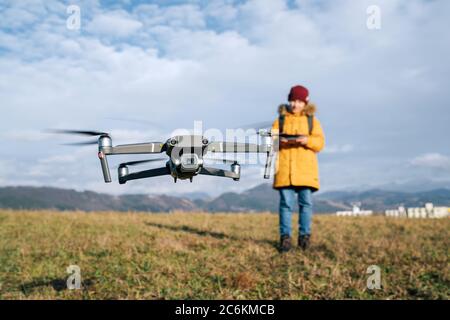 Close up image of flying drone with Teenager boy dressed yellow jacket  on background piloting a modern digital drone using remote controller Stock Photo