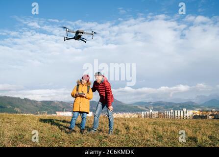 Father and Teenager boy son dressed yellow jacket piloting a modern digital drone using remote controller. Modern technology devises concept image Stock Photo