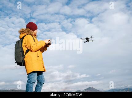 Teenager boy dressed yellow jacket piloting a modern digital drone using remote controller Stock Photo