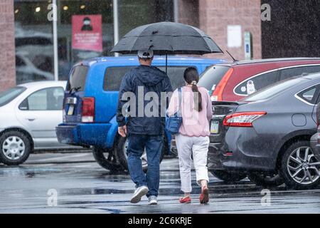 Couple walks in grocery store parking lot in the rain. Stock Photo