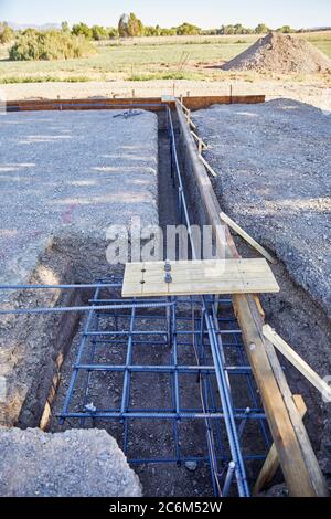 Level building site pad with three foot deep footing trench and concrete forms in place with copper ground wire for electric Stock Photo