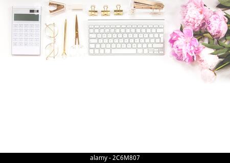 Keyboard, golden pen, glasses, calculator and a bouquet of pink peonies on a white background. Copy space. Stock Photo