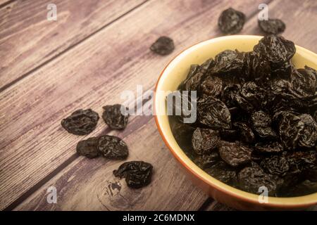 Dried prunes in a ceramic bowl and dried prunes scattered on a wooden background. Close up Stock Photo