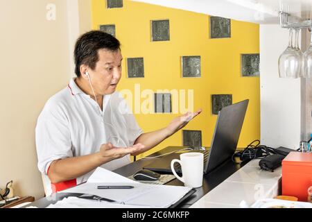 Matured Asian business man raises both hands in stressful expression in work from home video conference call Stock Photo